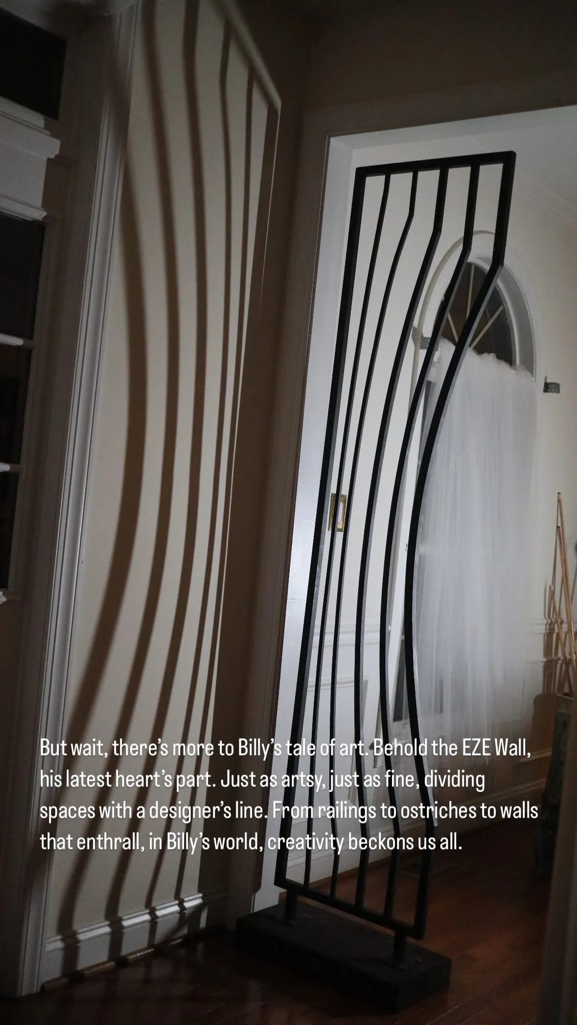 Modern black metal wall sculpture casting curved shadows on a white wall in a dimly lit room.