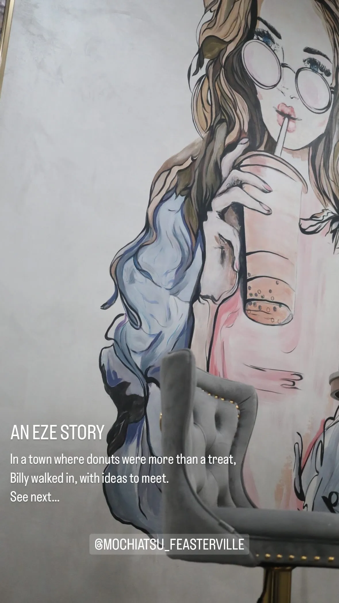 Mural of a woman with long hair and round glasses drinking bubble tea, next to a gray tufted chair and text about a story involving donuts and ideas.