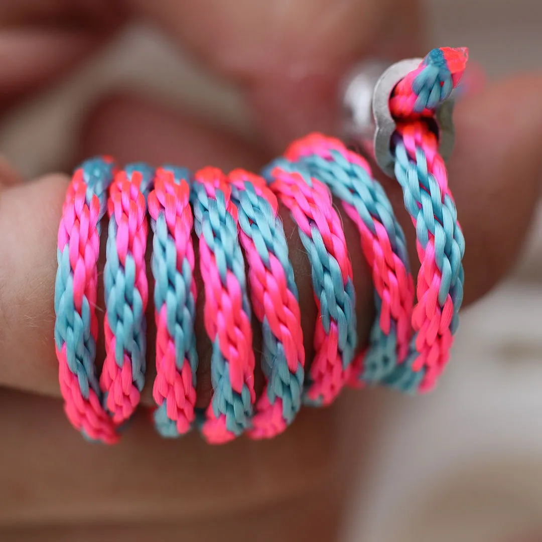 Close-up of a hand holding a coiled braided cord in bright pink and blue colors attached to a metal anchor.